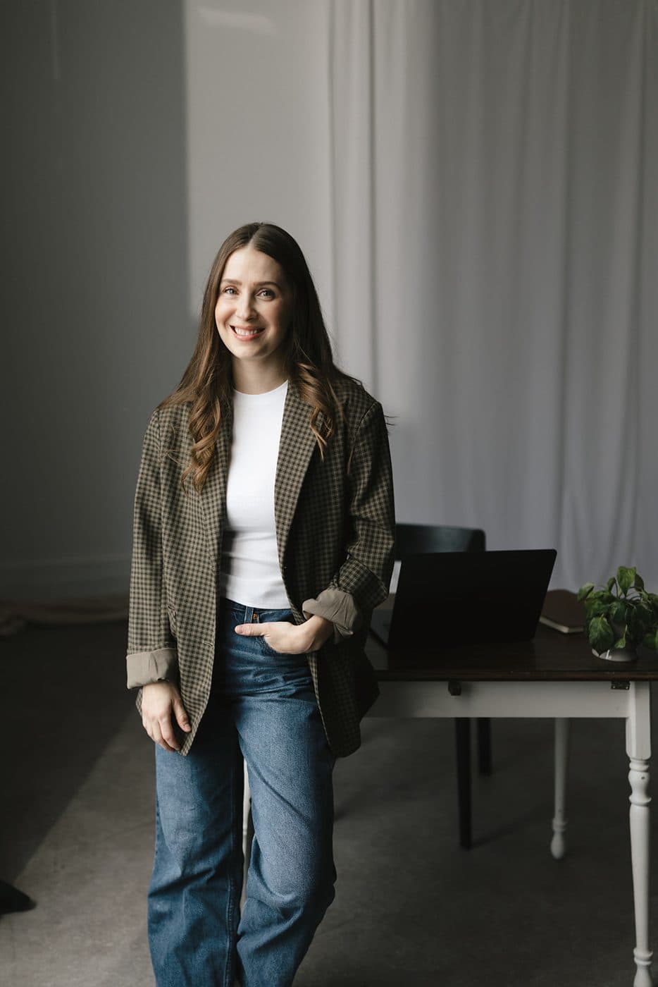 Sara standing by a window in an olive jacket