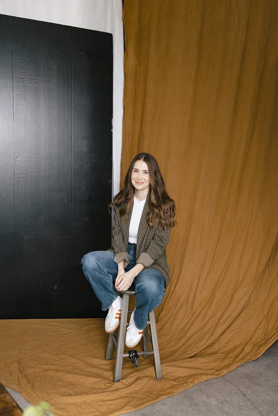 Sara sitting on a stool in front of a mustard backdrop
